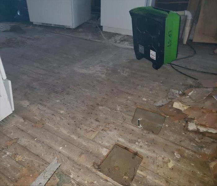 Dirty wooden flooring, some of which is torn up, with a dehumidifier in the background.