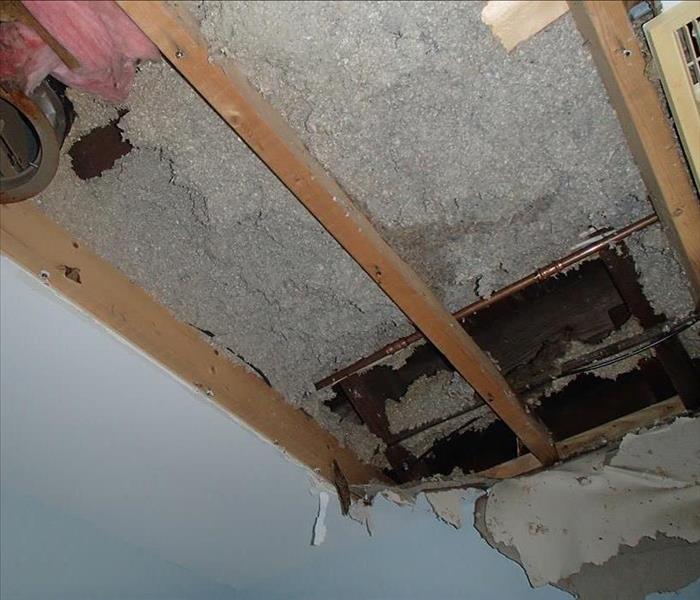 Ceiling with hole in it and exposed pipes following storm damage.