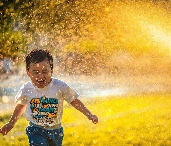 Young child in t shirt and jeans laughing and running through sprinkler.