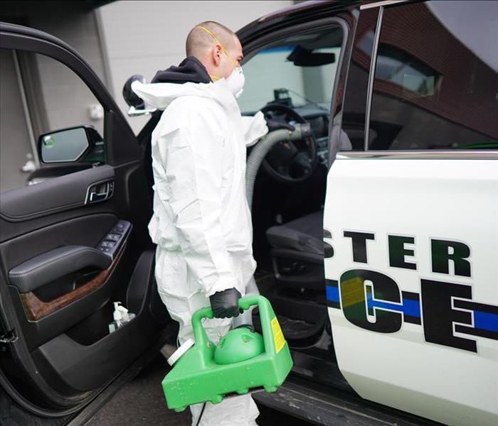 Male SERVPRO technician in Tyvek fogs a Lancaster Police vehicle with hospital-grade disinfectant.