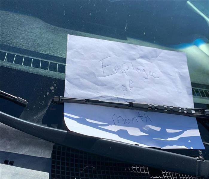 A paper with "Employee of the Month" written on it, tucked under a windshield wiper.