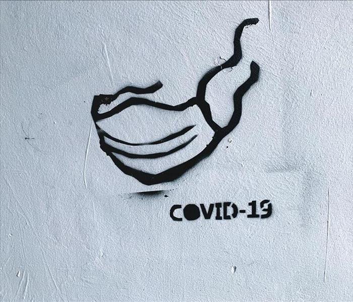 Face mask and text "COVID-19" spraypainted in black on white wall.